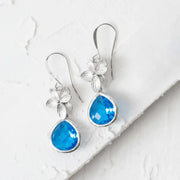 Blue teardrop earrings with floral designs on a white marble surface