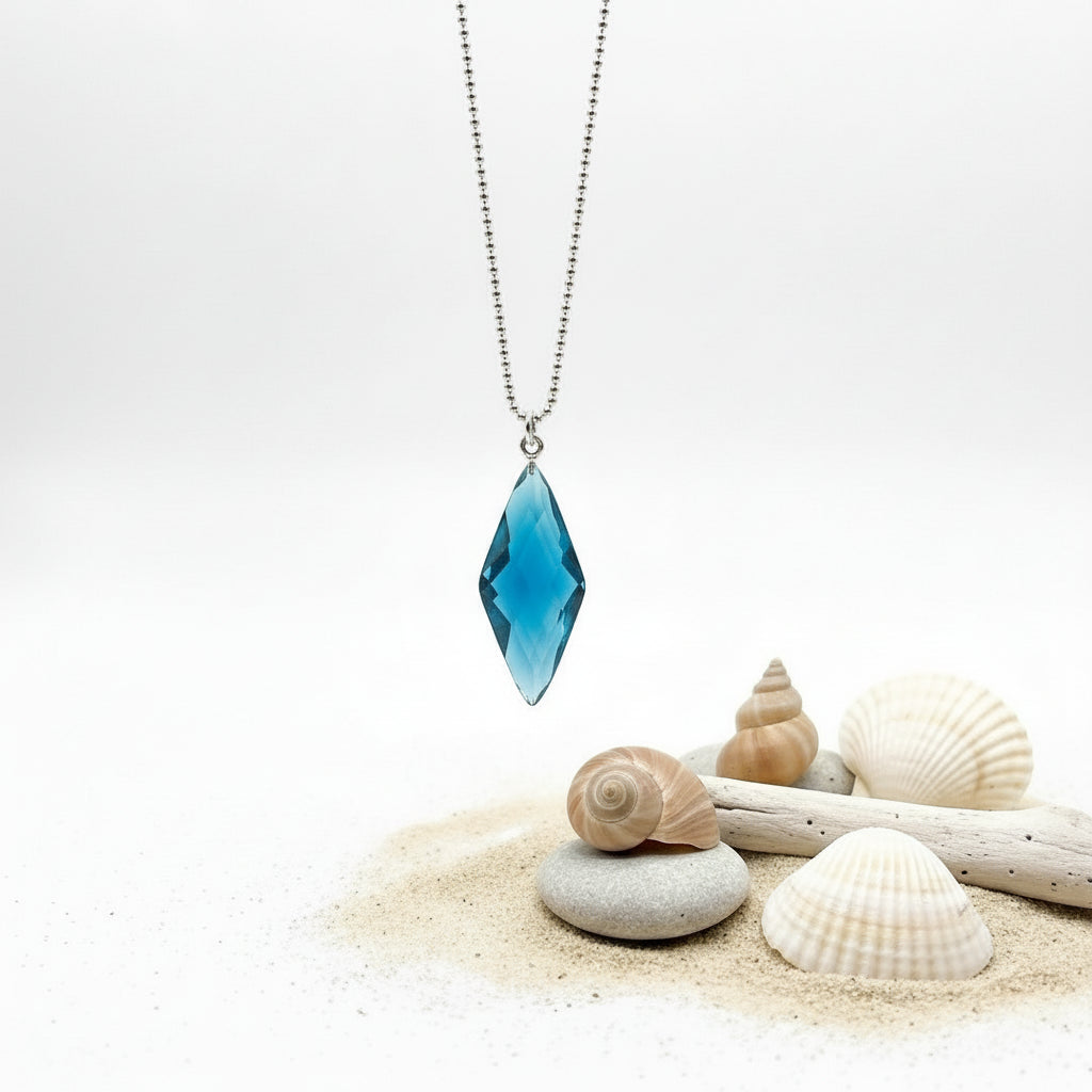 Blue pendant necklace on a white background with a gold rod and green leaves.