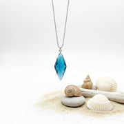Blue pendant necklace on a white background with a gold rod and green leaves.