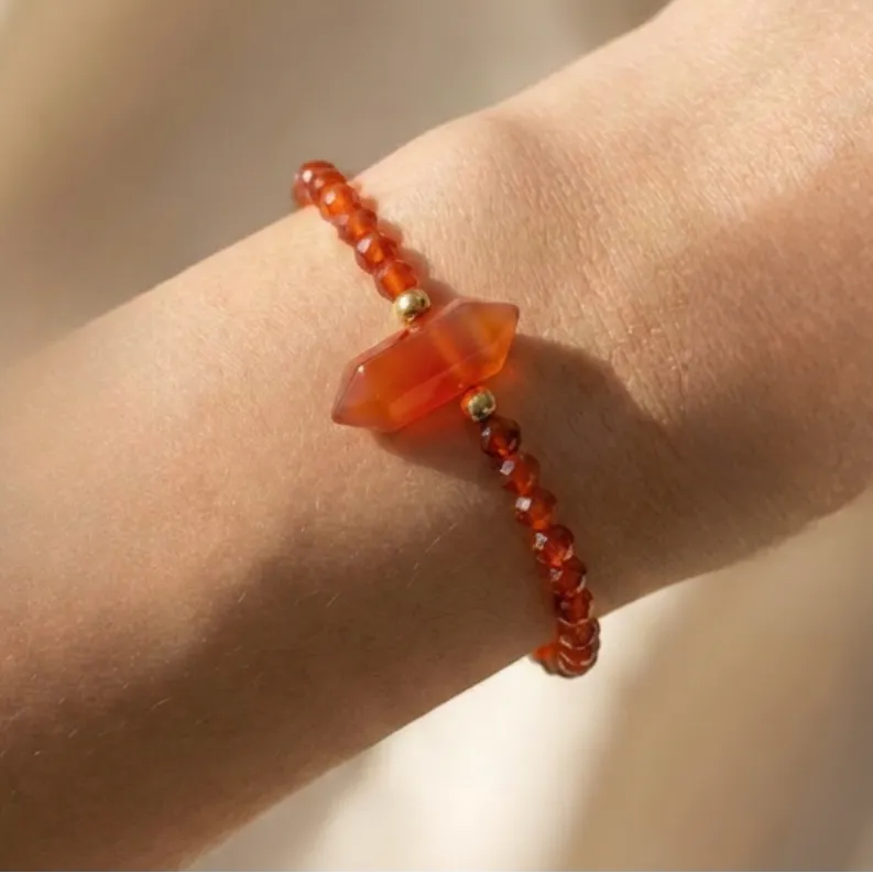 Orange beaded bracelet with a large orange stone on a wrist against a neutral background