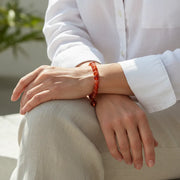 Person wearing a red beaded bracelet on a white shirt and beige pants.