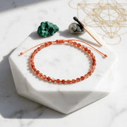 Orange beaded bracelet on a white marble surface with crystals and a crystal stick.