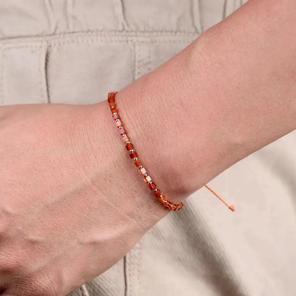 Close-up of a wrist wearing a red beaded bracelet on a neutral background