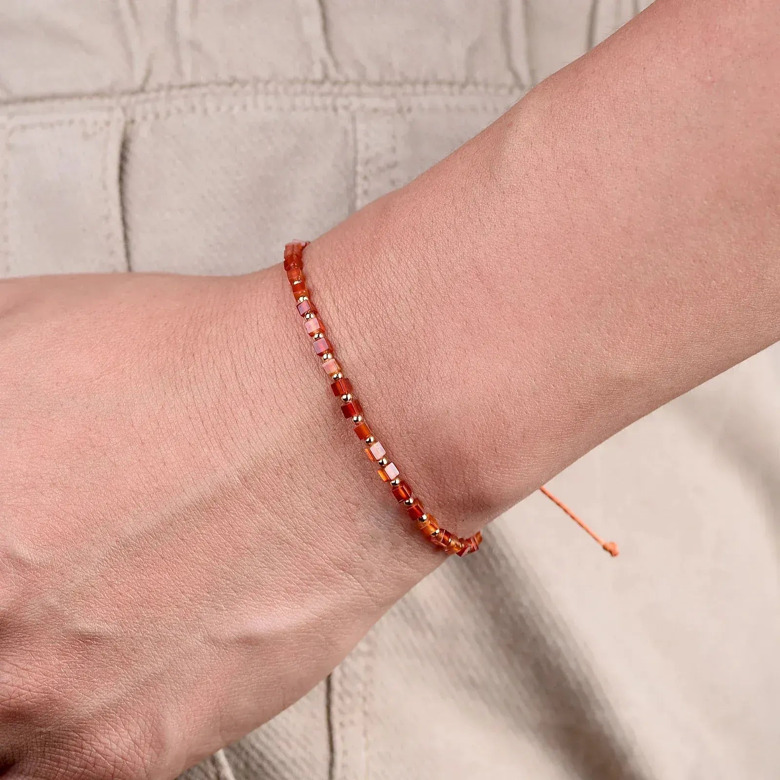 Close-up of a wrist wearing a red beaded bracelet on a neutral background