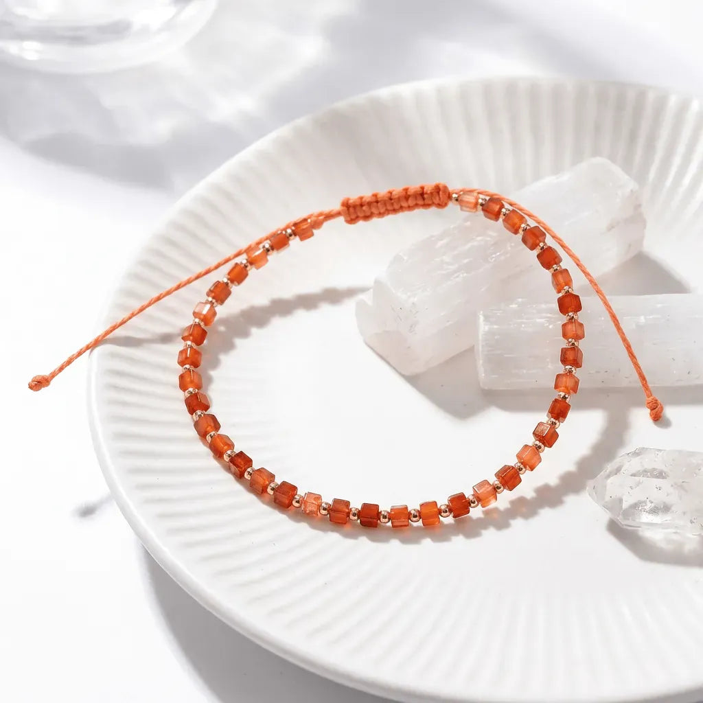 Orange beaded bracelet on a white plate with a shell and crystal