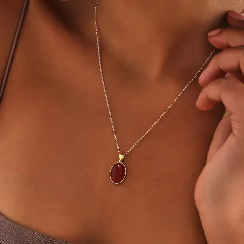 Necklace with a red pendant being worn on a person's neck.