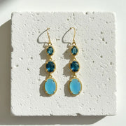 A pair of Mystic Soul dangle earrings with light blue and dark blue faceted gemstones in gold settings