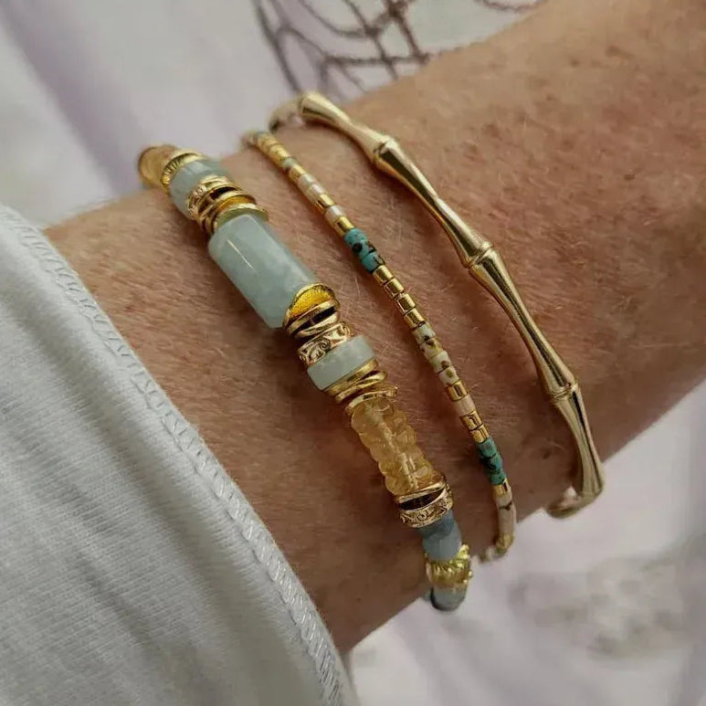 Close-up of a wrist wearing two gold and beaded bracelets on a neutral background