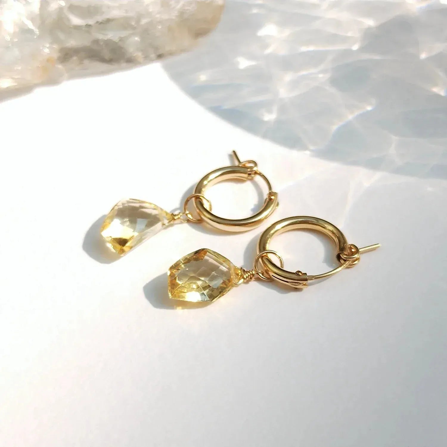 Gold hoop earrings with citrine stones on a light background