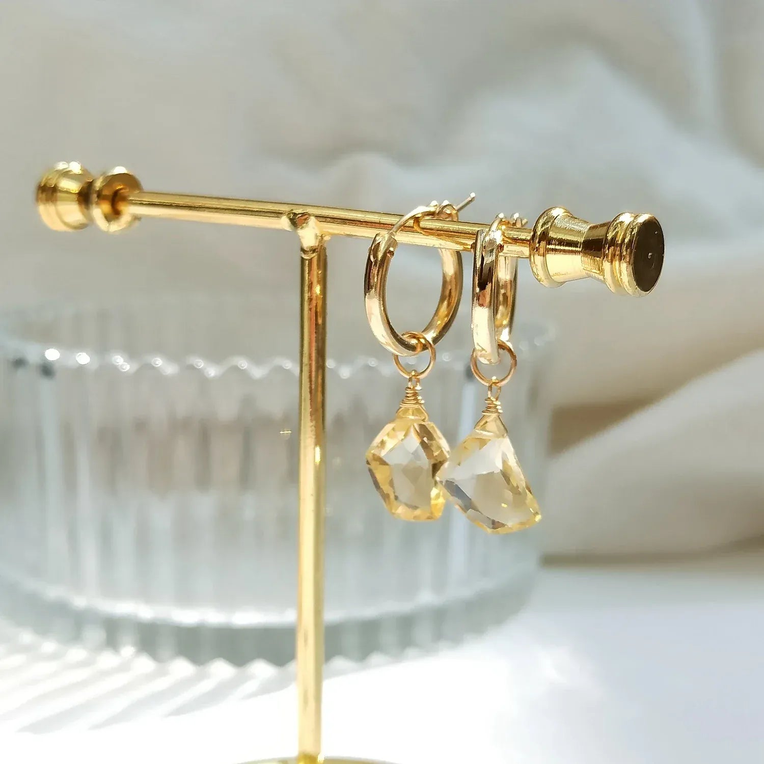 Gold hoop earrings with clear gemstones on a gold stand.