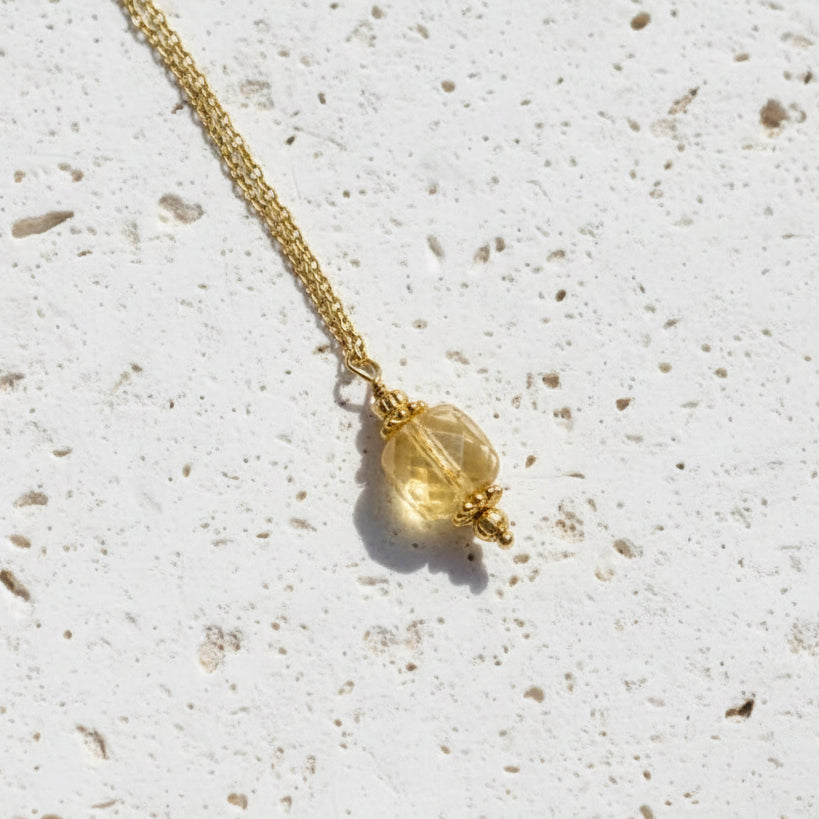 Gold necklace with a yellow gemstone pendant on a white background