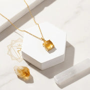 Gold necklace with a citrine pendant on a white surface