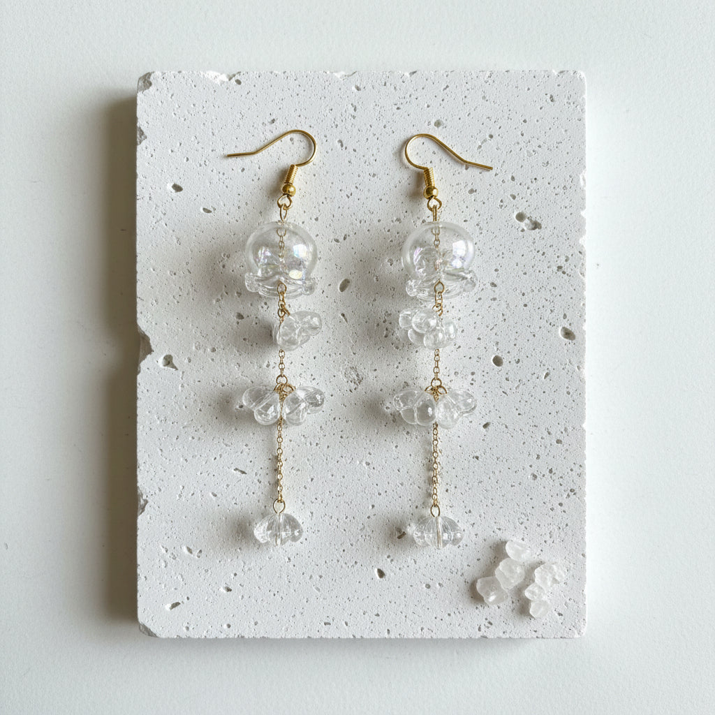 Clear glass jellyfish earrings with gold cascading florets on a white background