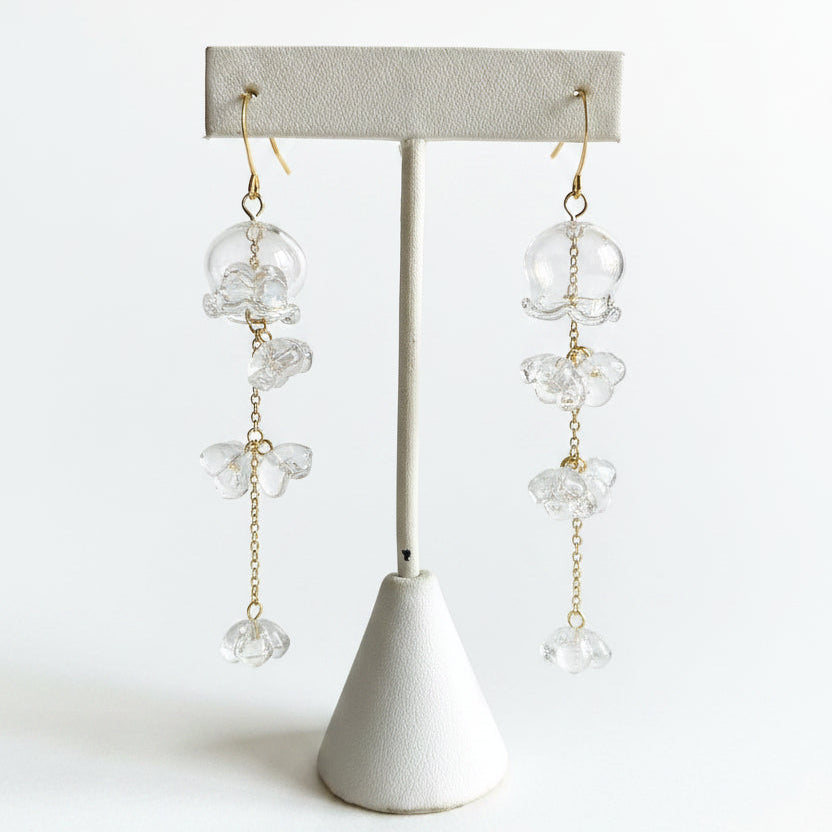 Clear glass jellyfish earrings with gold florets displayed on a jewelry stand