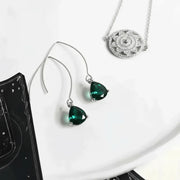 Green teardrop earrings on a white surface with a black book