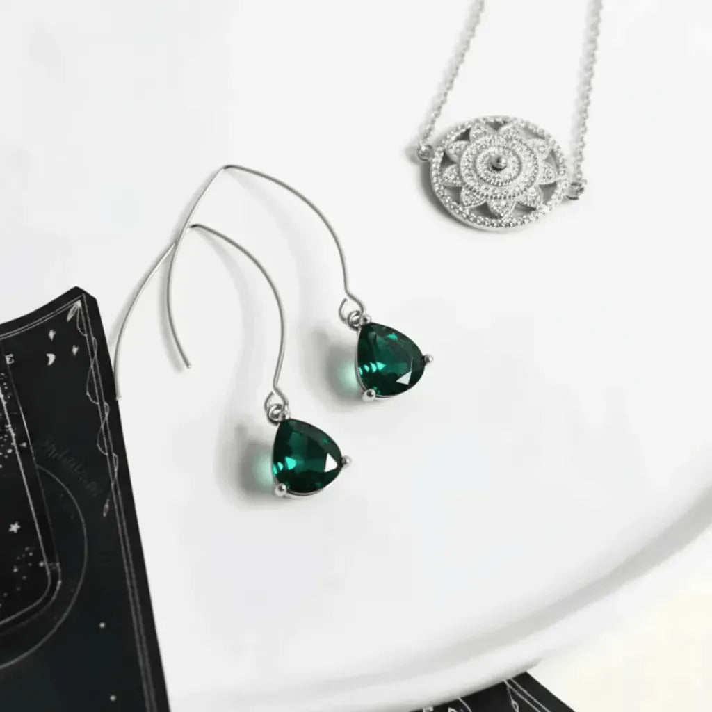 Green teardrop earrings on a white surface with a black book