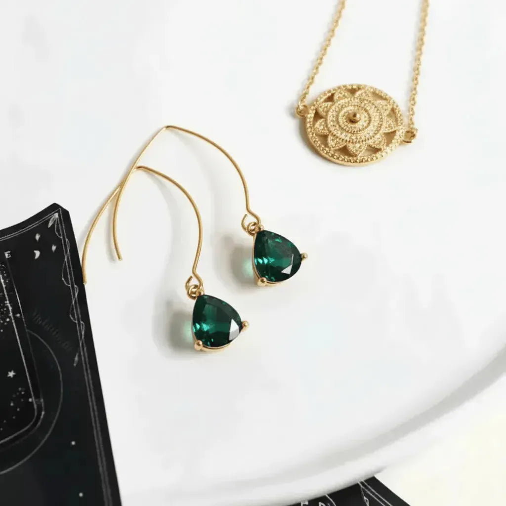 Gold earrings with green gemstones on a white plate