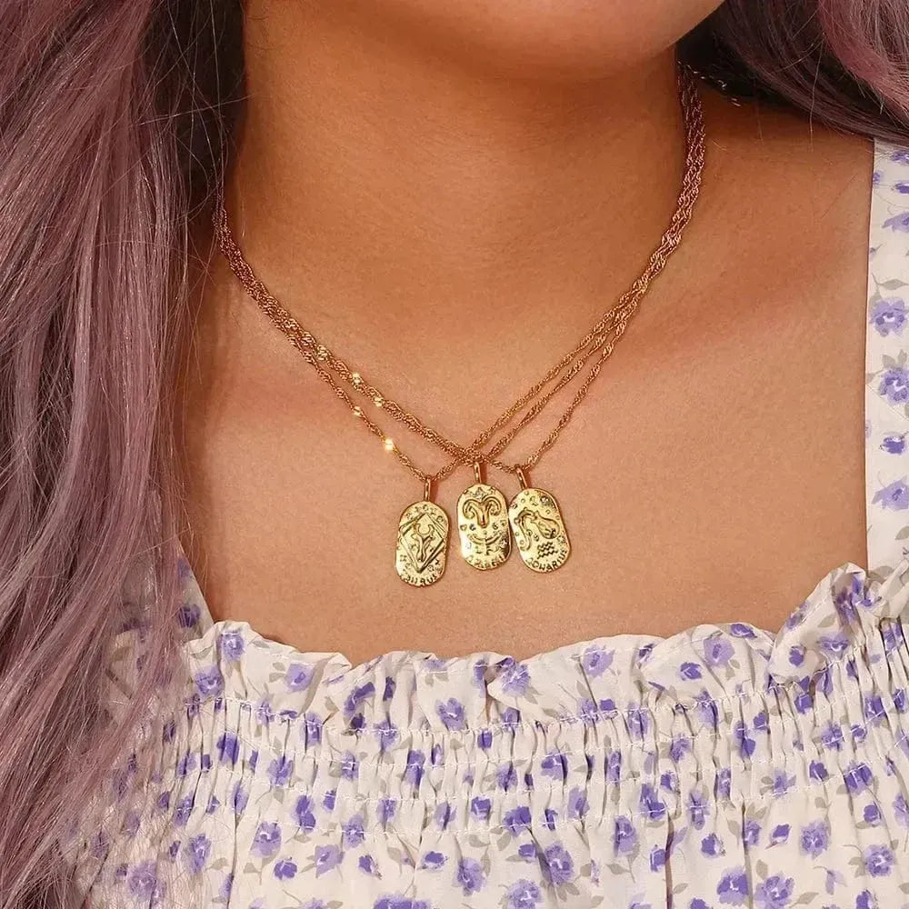 Close-up of a person wearing a gold necklace with three pendants, against a floral dress.