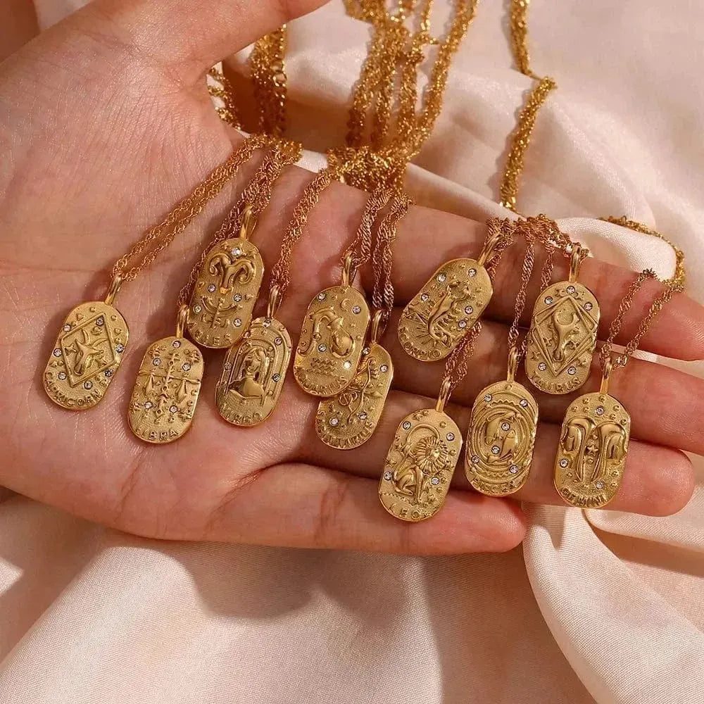 Gold necklaces with intricate pendants held in a hand against a beige background