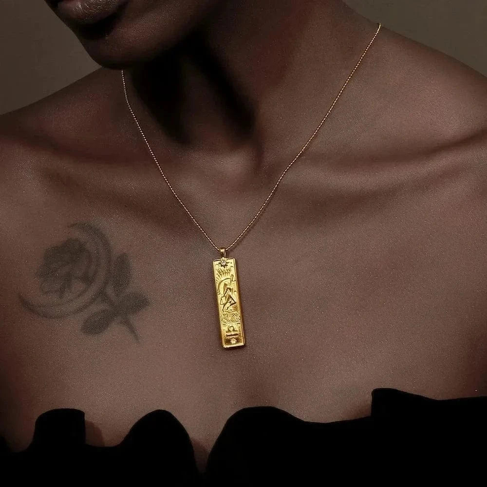 Gold necklace with a pendant on a person's neck against a brown background