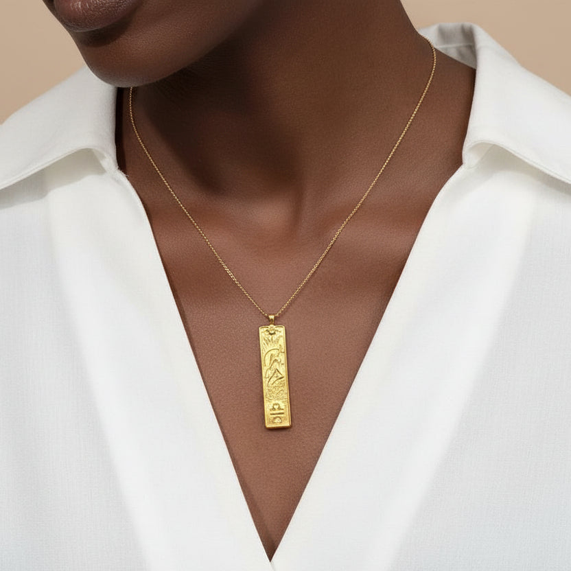 Gold necklace with a pendant on a person's neck against a brown background