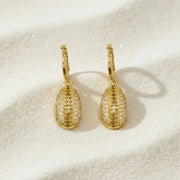 Gold earrings with intricate designs on a beige surface