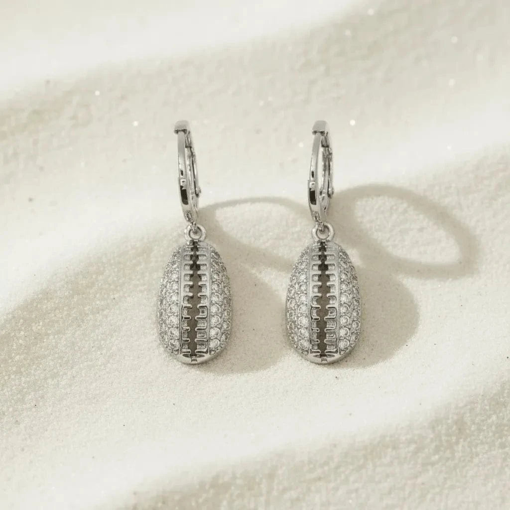 Silver football-shaped earrings on a textured beige surface