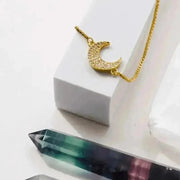 Gold necklace with a crescent moon pendant on a white surface