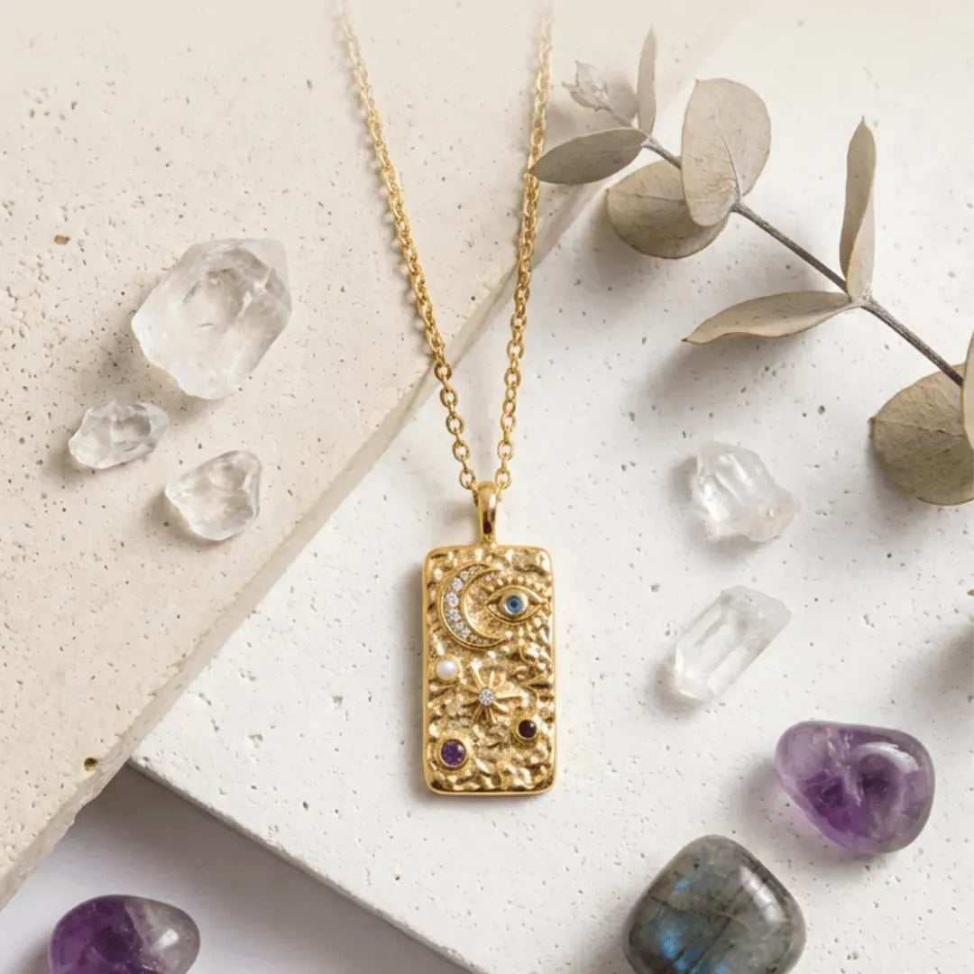 Gold necklace with a decorative pendant on a textured surface with crystals and leaves.