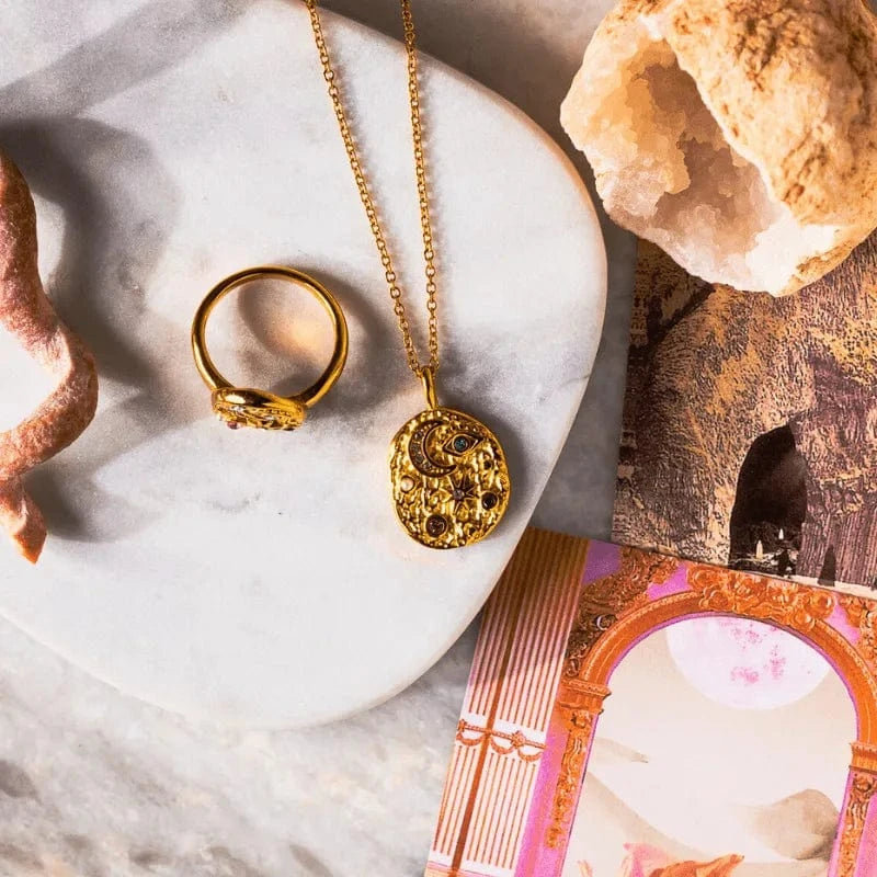 Gold necklace and ring on a marble surface with crystals and a book