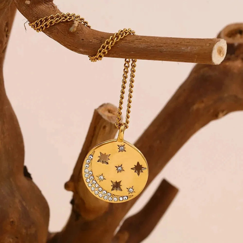 Gold necklace with a circular pendant featuring stars and moons, hanging on a wooden branch.