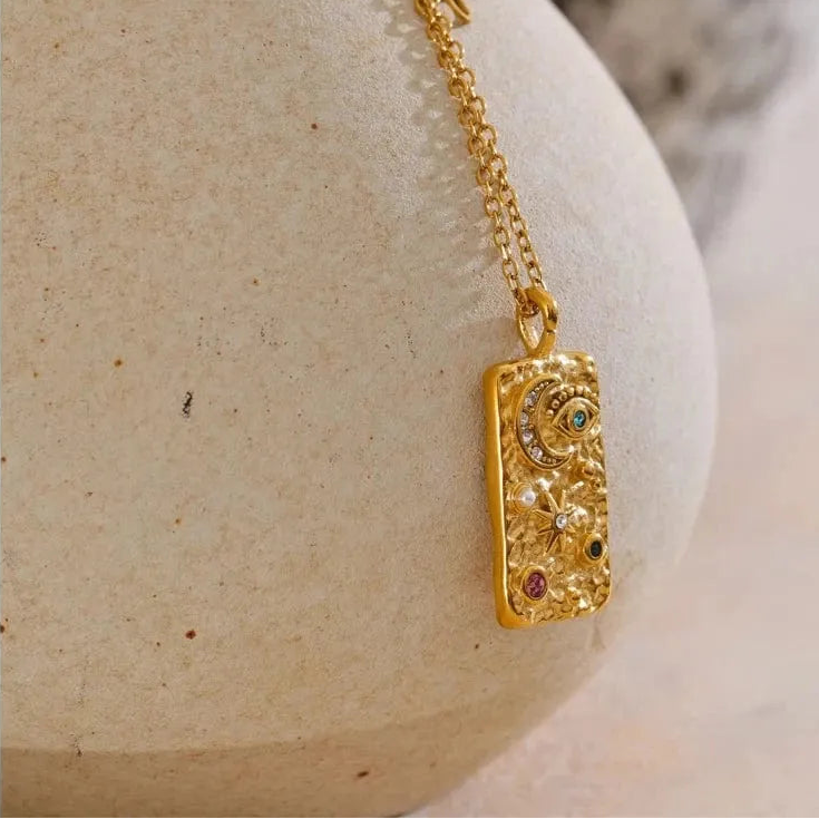 Gold necklace with a pendant on a beige stone surface
