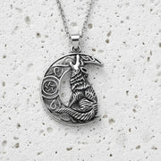 Silver pendant with a wolf design on a textured white surface