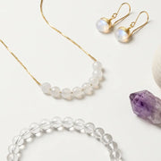 Jewelry set including necklace, earrings, and bracelet on a white surface with a crystal and small container.
