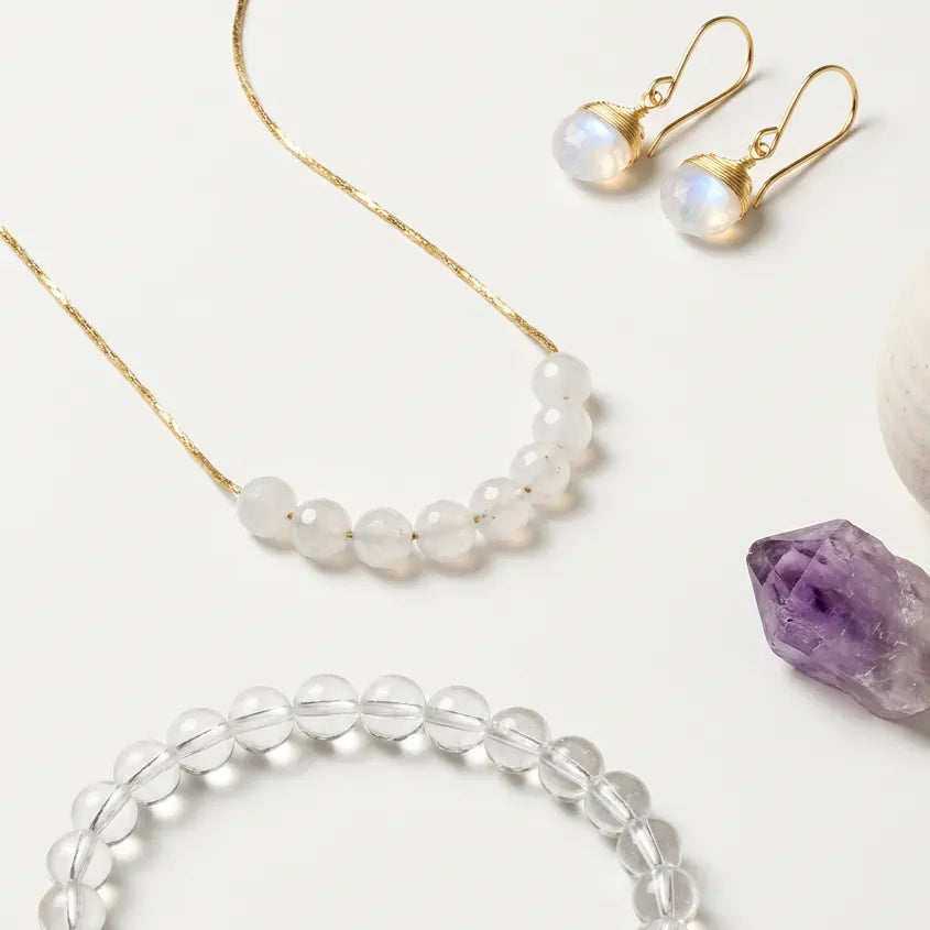 Jewelry set including necklace, earrings, and bracelet on a white surface with a crystal and small container.