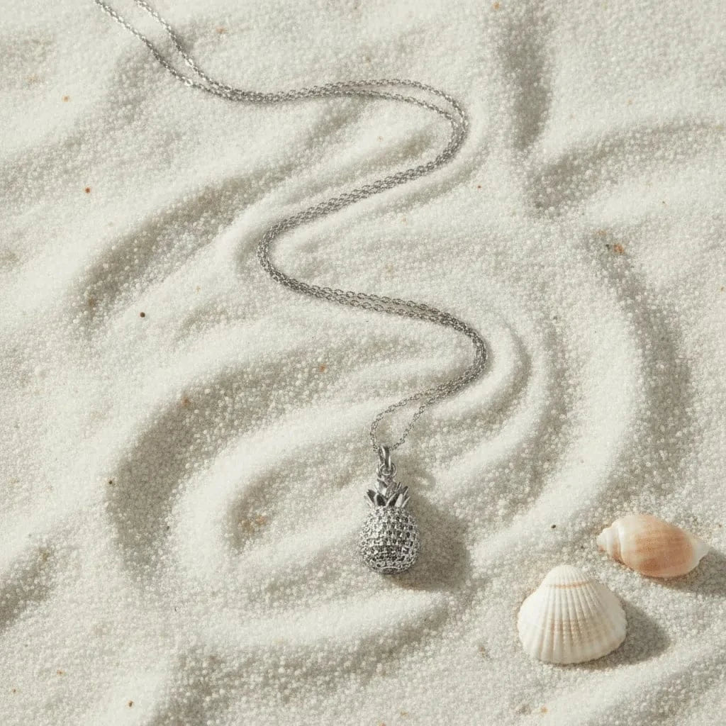 Silver necklace with a pineapple pendant on sand with two shells