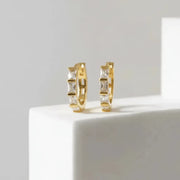 Gold hoop earrings with square-cut gemstones on a white surface