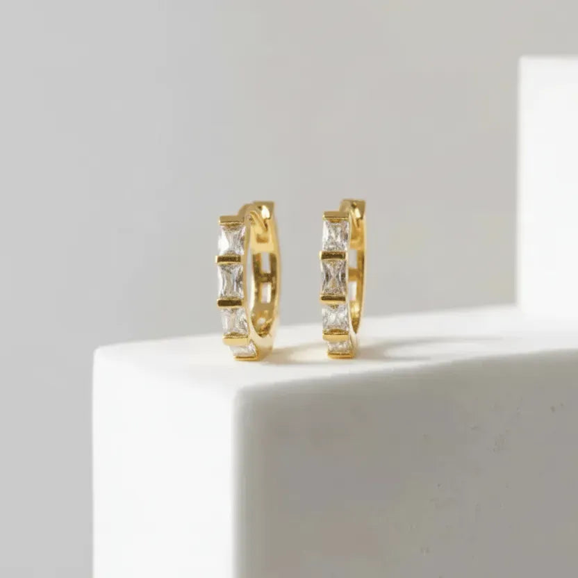 Gold hoop earrings with square-cut gemstones on a white surface