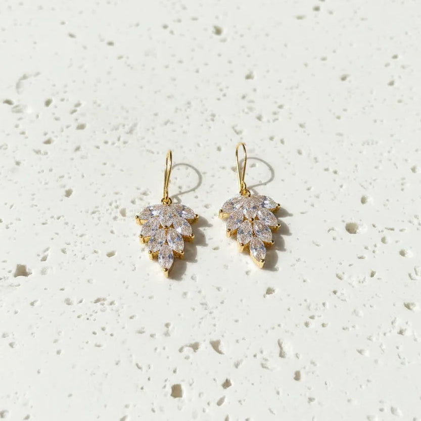 Gold earrings with clear gemstones on a textured white surface