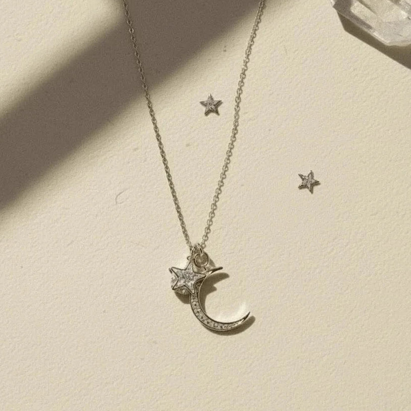 Silver necklace with moon and star pendants on a beige surface