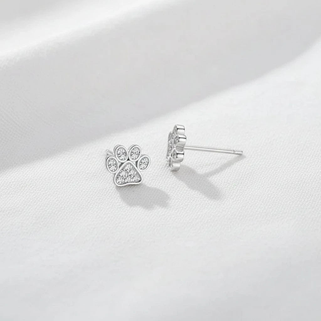 Silver paw print earrings on a blue surface