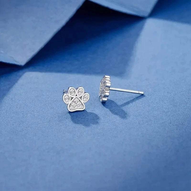 Silver paw print earrings on a blue surface