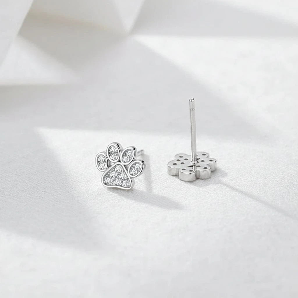 Silver paw print earrings on a blue fabric background