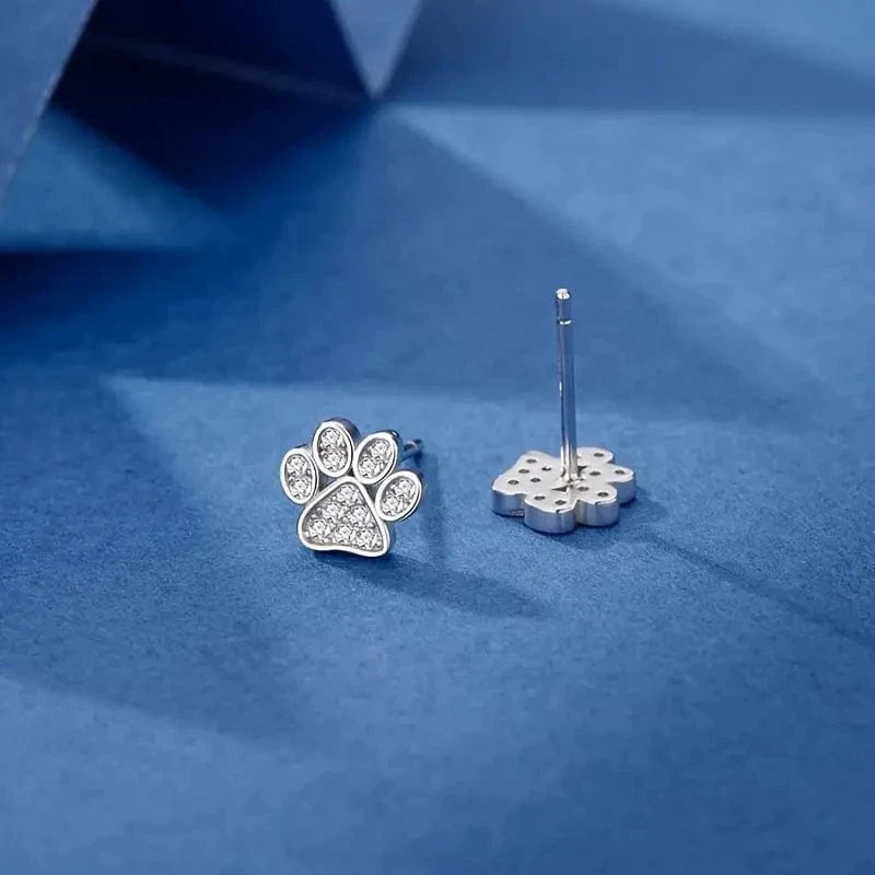 Silver paw print earrings on a blue fabric background