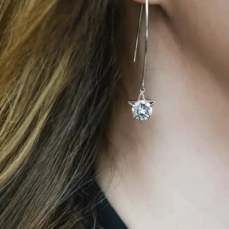 Silver earring with a clear gemstone worn by a person with brown hair.