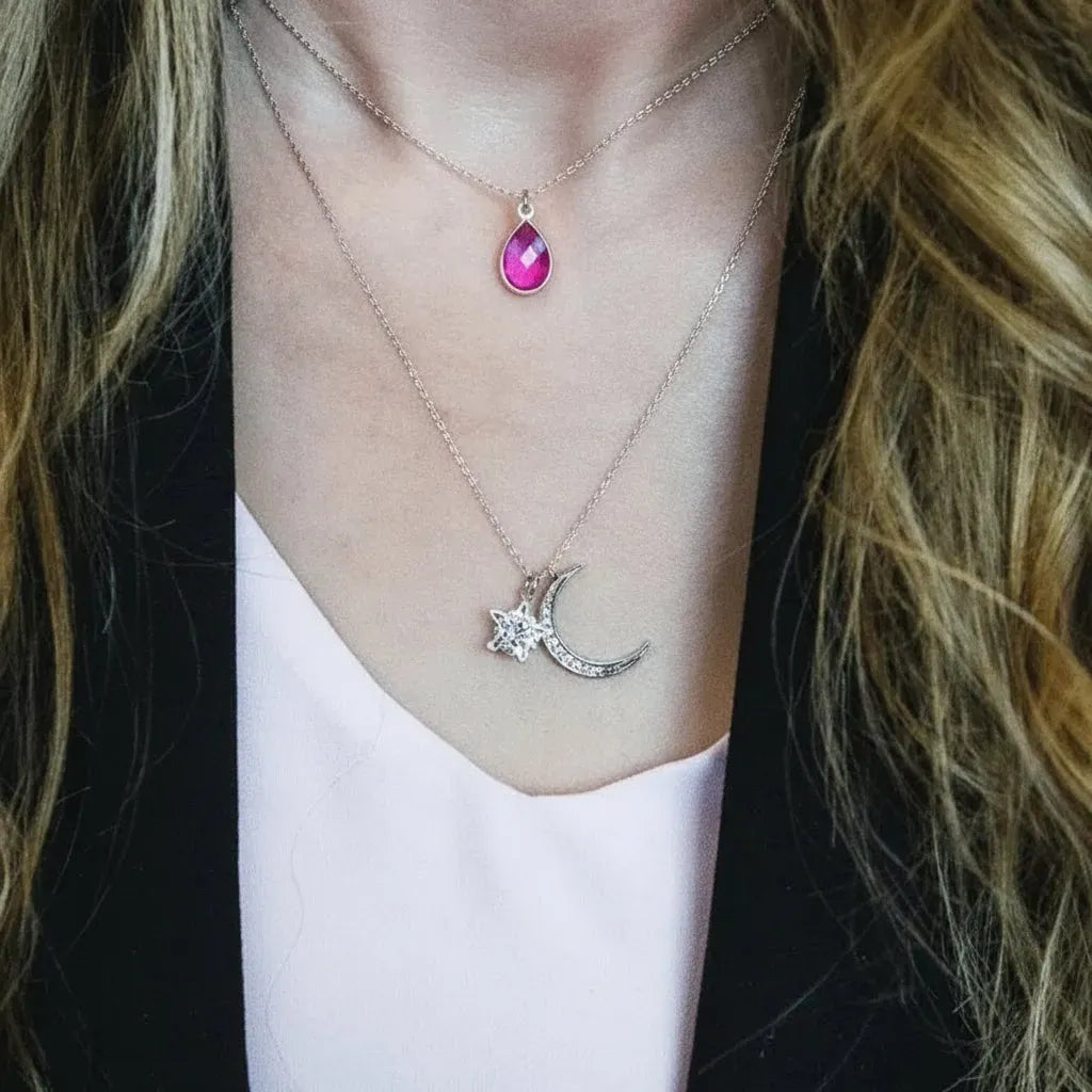 Necklace with pink gemstones and a moon and star pendant on a person wearing a white top.