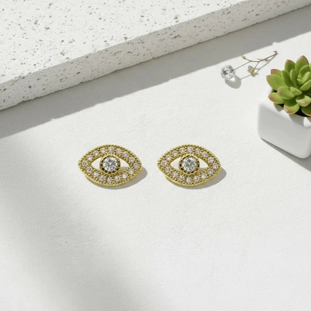 Gold eye-shaped earrings with clear gemstones on a light background