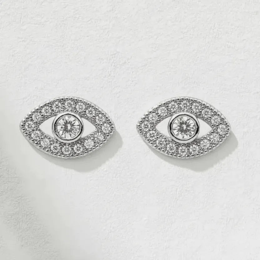 Pair of silver eye-shaped earrings with clear gemstones on a light gray background
