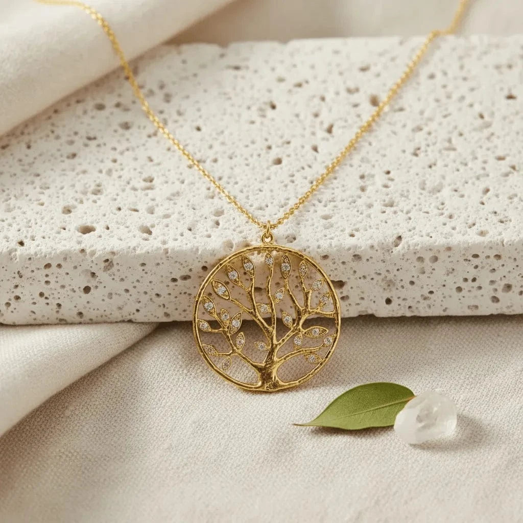 Gold necklace with a tree-shaped pendant on a textured surface with a leaf and stone.