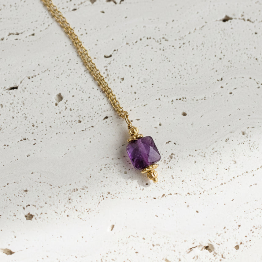 Gold necklace with a purple gemstone pendant on a white background